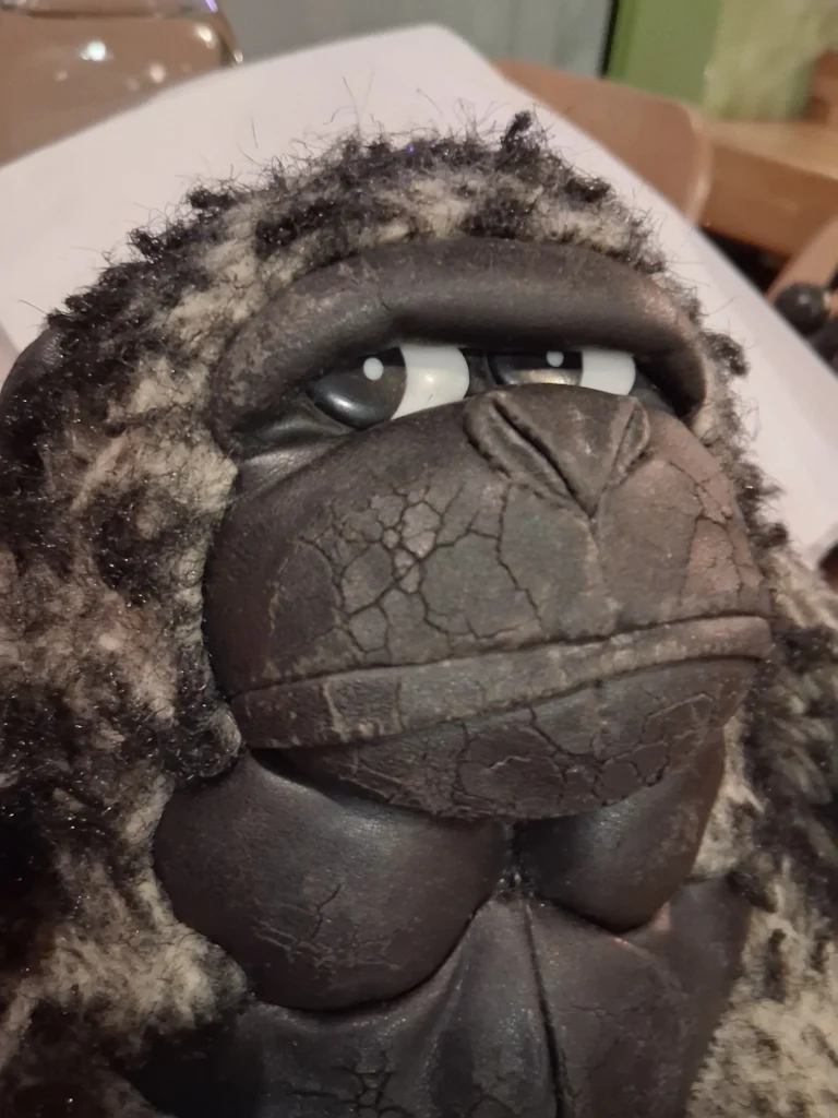 Κοντινή λήψη του προσώπου του Monkey πριν από την αποκατάσταση, όπου διακρίνεται η φυσική φθορά του συνθετικού δέρματος από το πέρασμα του χρόνου.